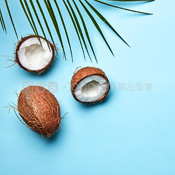 整個和一半的椰子,在藍色背景上的棕櫚葉和文本空間的副本。一個奇異的水果。扁平放。一個椰子和棕櫚綠葉在藍色背景上的副本空間。熱帶堅果。扁平放。